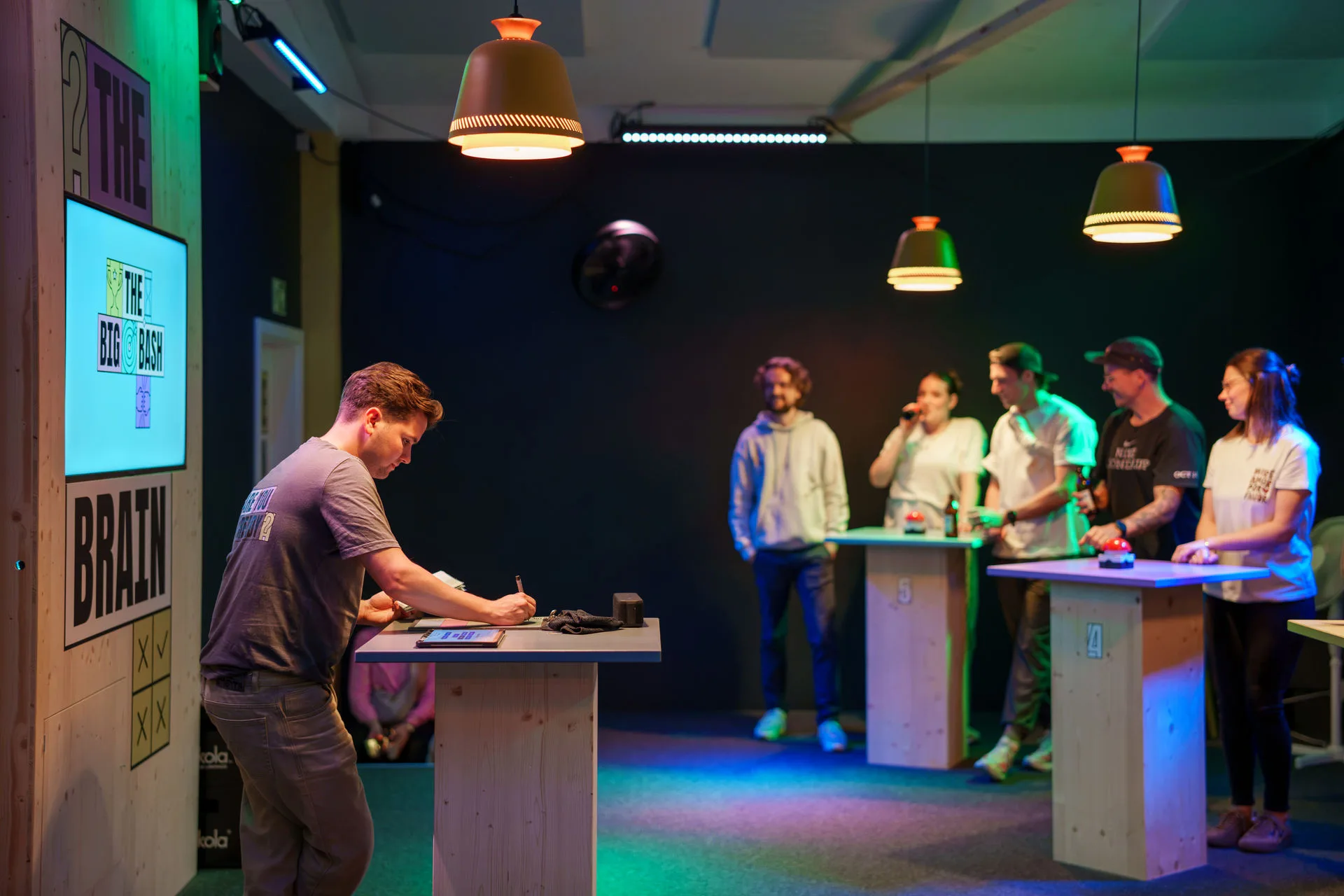 Gameshow-Moderator notiert Punkte im Quizraum The Brain, im Hintergrund spielen die Teams